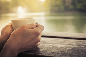 Closeup on a woman's hands holding a cup of tea by a lake in the afternoon