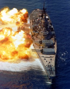 A bow view of the battleship USS IOWA (BB-61) firing its Mark 7 16-inch/50-caliber guns off the starboard side during a fire power demonstration.
